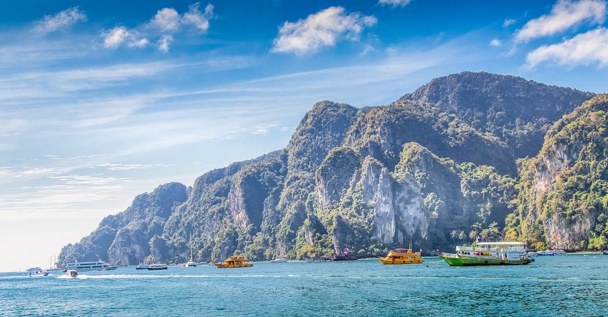 Bunte Boote vor den Kalksteinklippen von Koh Phi Thailand bei strahlend blauem Himmel und ruhiger See.