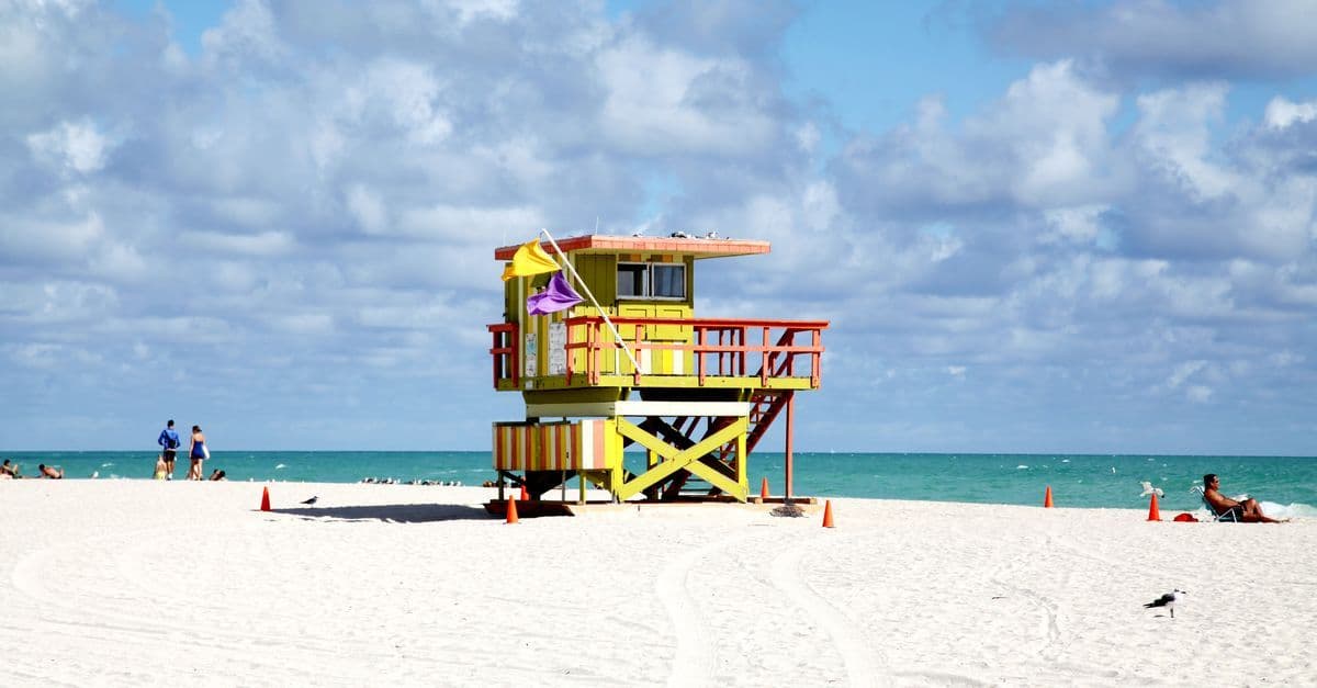 Una torretta di salvataggio colorata sulla spiaggia di Miami Beach, con il mare turchese e pochi bagnanti.