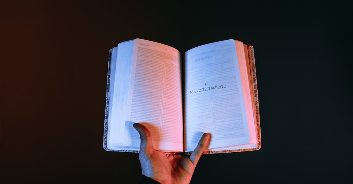 Mano sosteniendo una Biblia abierta en el Nuevo Testamento sobre fondo oscuro.