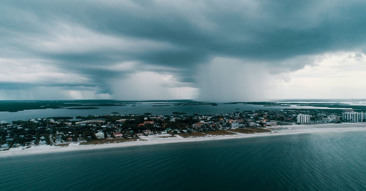 Nuvole temporalesche e pioggia incombono sulla costa di Miami, tra spiaggia, mare e case.