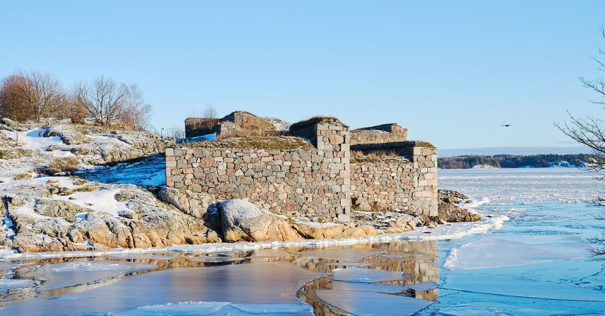 冬日陽光下,赫爾辛基海岸的石造建築旁覆著積雪,海面結冰,呈現寒冷的天氣景象。