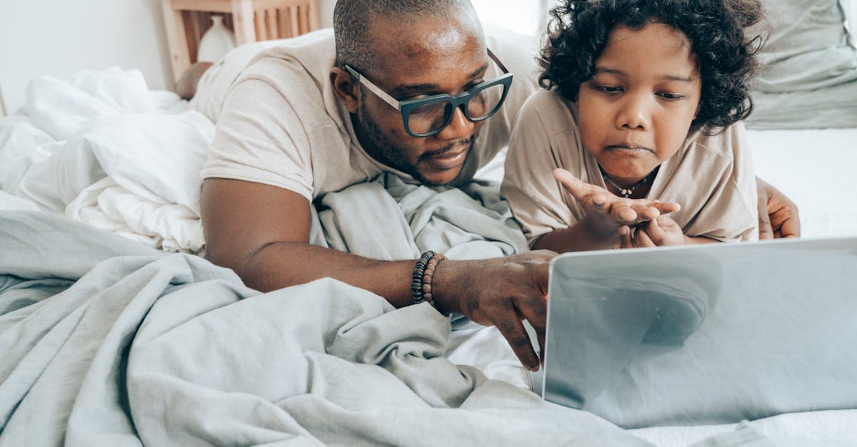 Father and young child sharing a laptop in bed, connected via portable wifi during a family holiday