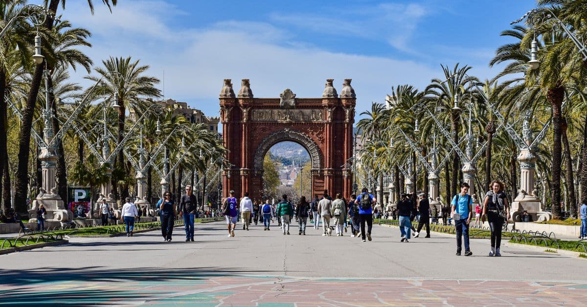 Locals and visitors strolling through sun-dappled parkland near Arc de Triomf during the ideal Barcelona holiday season.