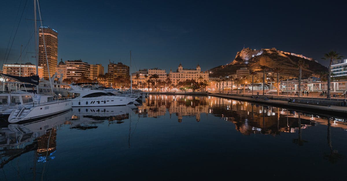 Upplyst hamn i Alicante nattetid med utsikt mot Santa Bárbara-slottet, nära Alicante airport.