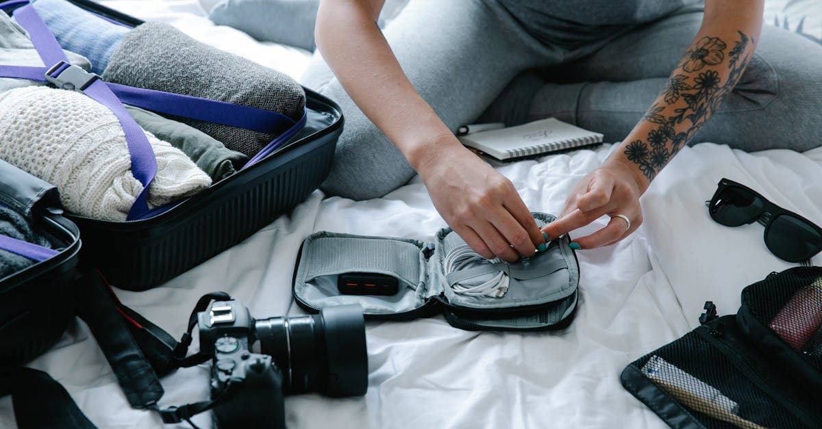 Frau mit Tattoos packt Koffer und Technik-Gadgets – Kleidung in der Reise-Checkliste organisieren