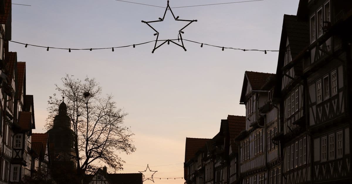 Historic European street at dusk with half-timbered buildings and star-shaped holiday lights overhead.