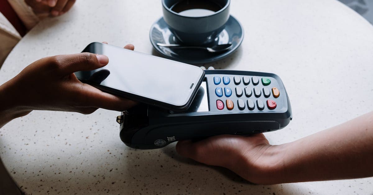 A person using a smartphone to make a contactless payment with a card reader on a cafe table.
