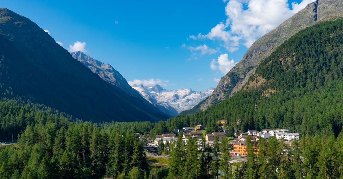 Malerisches Dorf Pontresina in den Schweizer Alpen mit üppigem Grün und strahlend blauem Himmel.