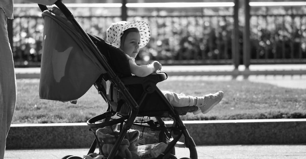 Baby wearing a sun hat sits in a stroller on a monochrome urban street