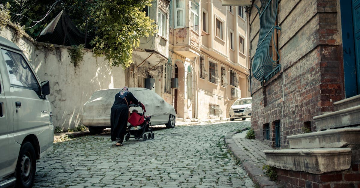 Woman pushes a travel stroller up a cobblestone street in a sunlit European neighbourhood
