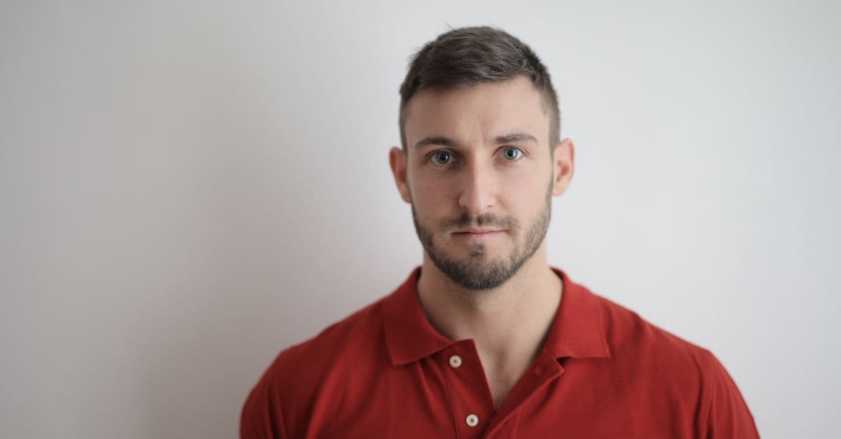 Head-and-shoulders photo of a man in a red polo shirt facing the camera against a plain white wall.