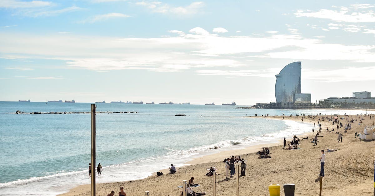 Turyści wypoczywający na tłocznej plaży Barceloneta w słońcu, ciesząc się aktywnościami plażowymi podczas wakacji w Barcelonie.