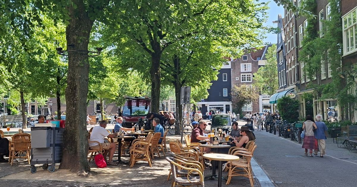 Gepensioneerde geniet van een ontspannen zomermiddag op een Amsterdams terras tijdens verblijf in het buitenland.