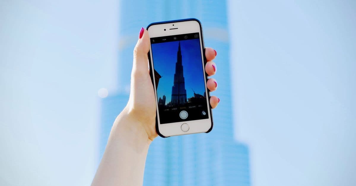 Mano con smartphone che fotografa il Burj Khalifa a Dubai, connessione eSIM travel.