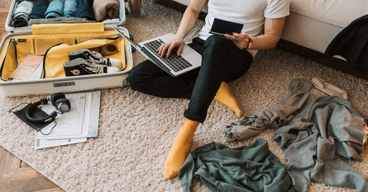 Mann packt Koffer und nutzt Laptop für günstige Internetlösungen auf Auslandsreisen