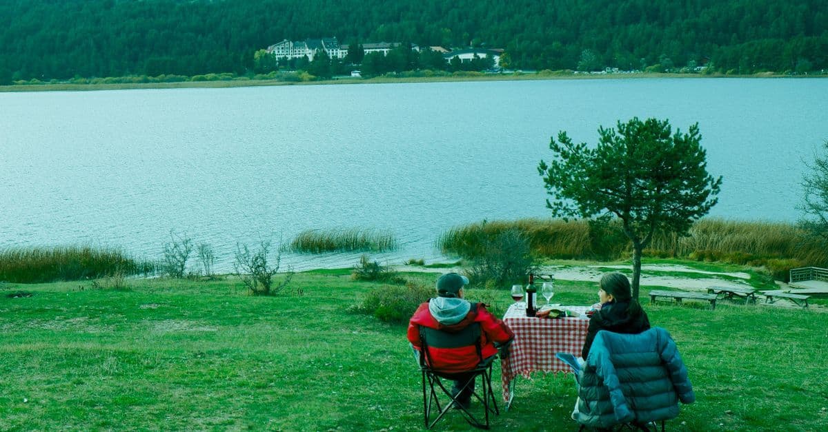 Paar beim romantischen Picknick am Seeufer mit Wein – Erlebnisse als Muttertagsgeschenk 2025 schaffen unvergessliche Erinnerungen.