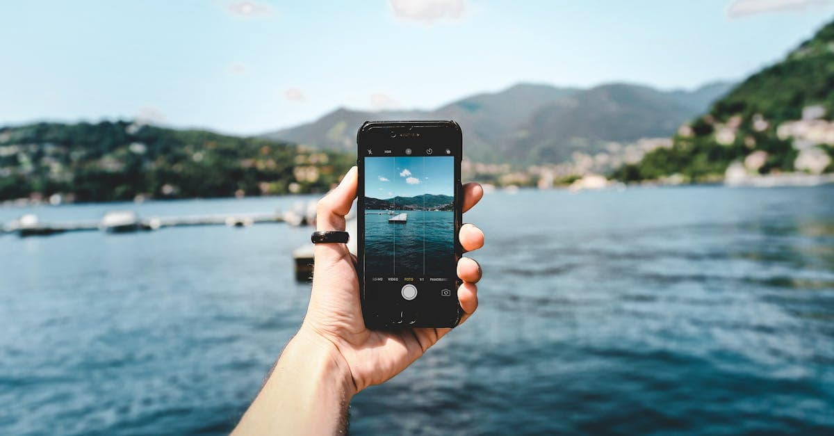 Pessoa fotografando belo lago com smartphone ao ar livre, aprendendo a habilitar o roaming internacional no celular