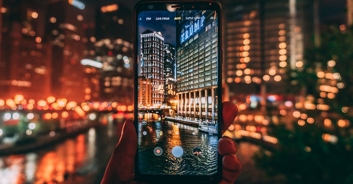 Traveler holding a smartphone to photograph the illuminated Chicago skyline and Trump Tower at night.