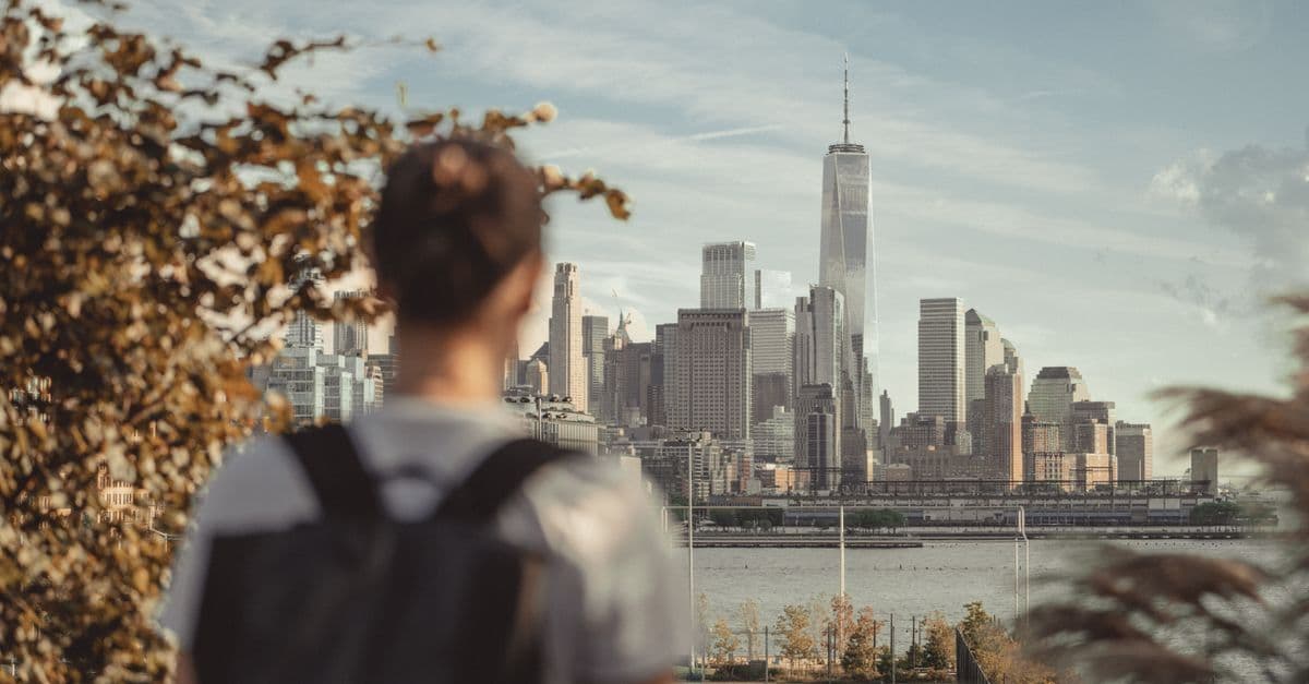 En resenär med ryggsäck blickar ut över Manhattans skyline i New York från andra sidan floden.