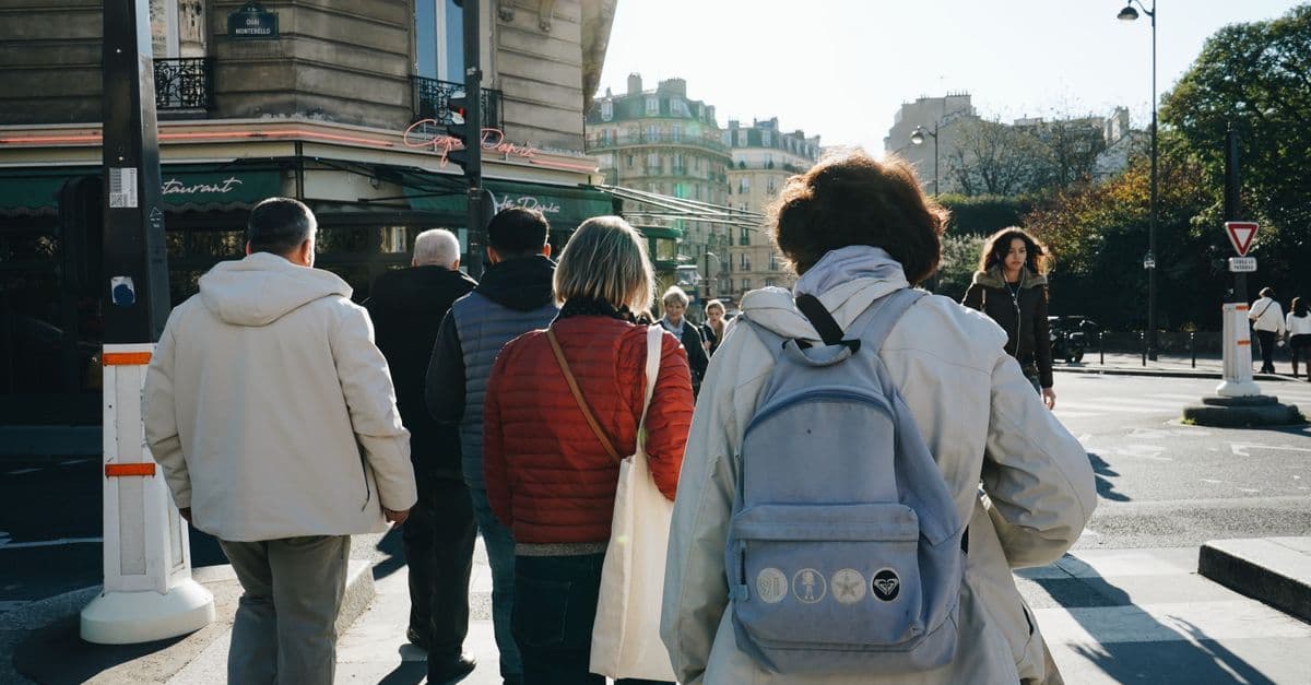 People cross a sunny street corner in Paris on an autumn day, past a café with green awnings.