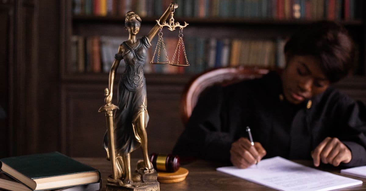 Geconcentreerde rechter schrijft documenten naast een Vrouwe Justitia-standbeeld, symbool voor lalabet reviews betrouwbaarheid in Nederland.