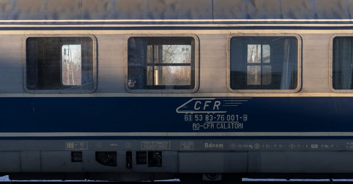 Blue passenger train carriage with three windows lit by low sun at a station platform.