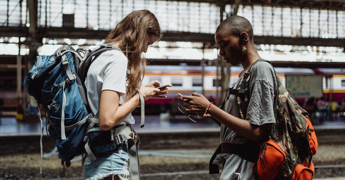 Zwei Reisende nutzen ihre Smartphones am Bahnhof, um Roaming-Kosten auf ihrer 12 Travel Reise zu prüfen.