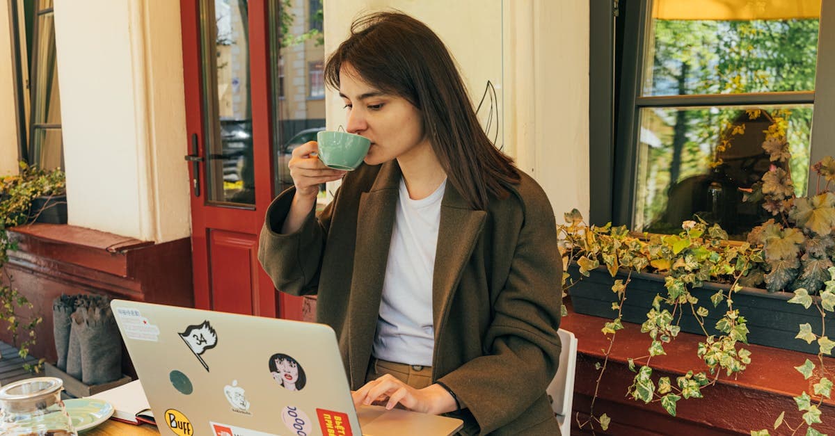 Ung kvinna dricker kaffe och jobbar på laptop på uteservering – viktig uppkoppling för den som vill jobba utomlands