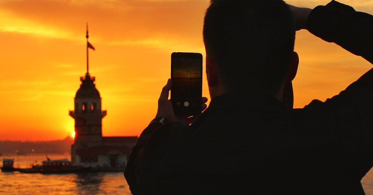 İstanbul'da Kız Kulesi gün batımını fotoğraflayan bir kişinin silueti Türkiye seyahat deneyimini yansıtıyor