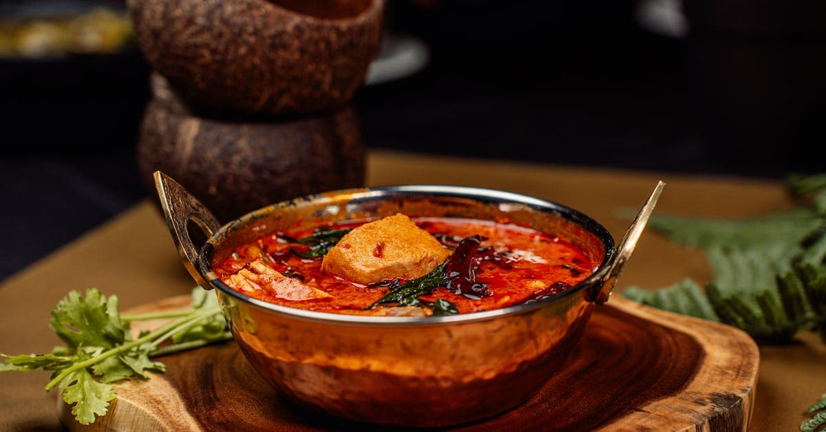 Curry auténtico de gastronomía india servido en recipiente de cobre tradicional sobre tabla de madera