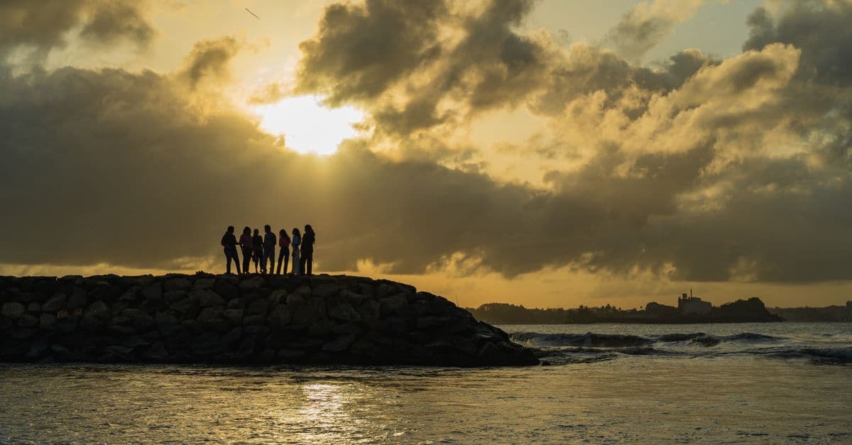 Silhouetted travellers watching a golden sunset on Galle Beach, Sri Lanka