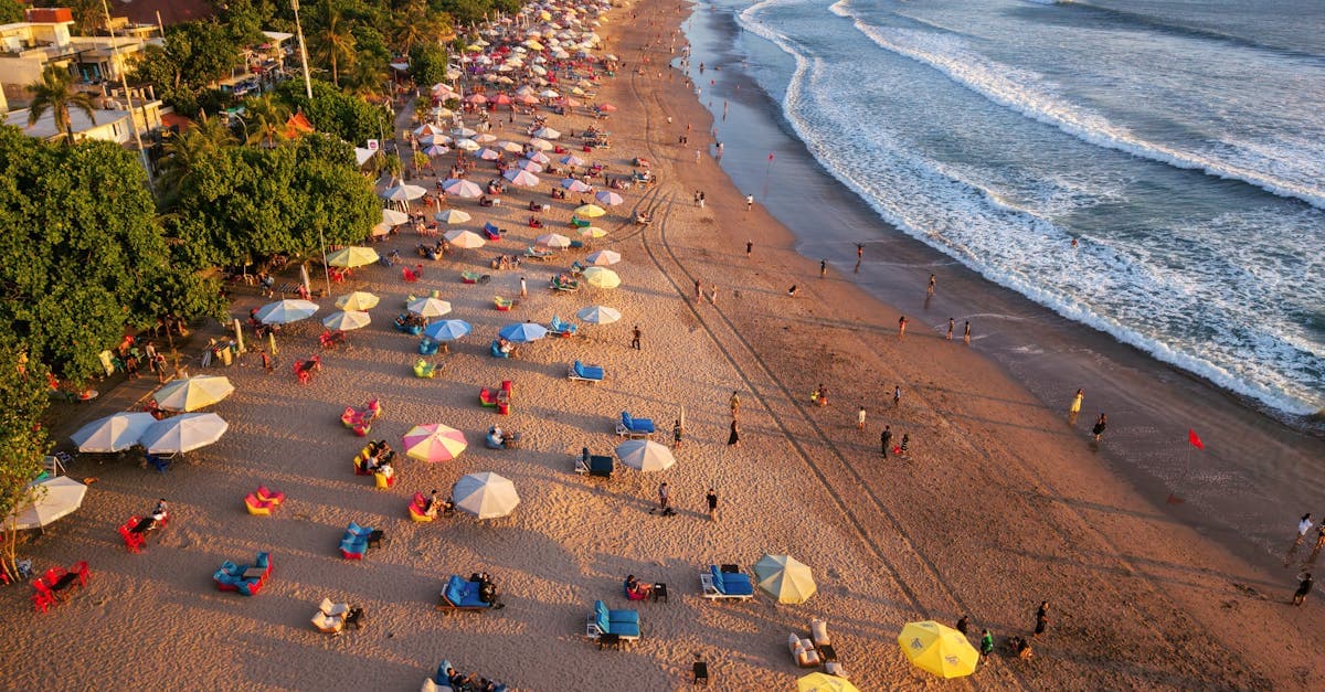 Aerial shot of lively beach with colorful umbrellas and ocean waves in Bali, Indonesia.