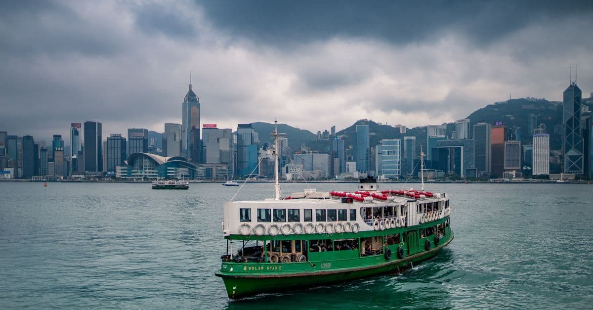 A green-and-white ferry crosses the harbor in front of Hong Kong's dense waterfront skyline.
