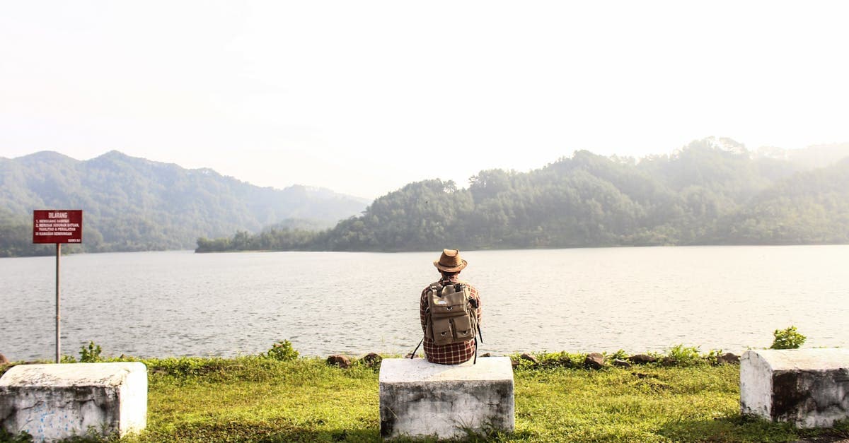 Lone traveler by calm mountain lake, reflecting on traveling alone tips for handling travel emergencies