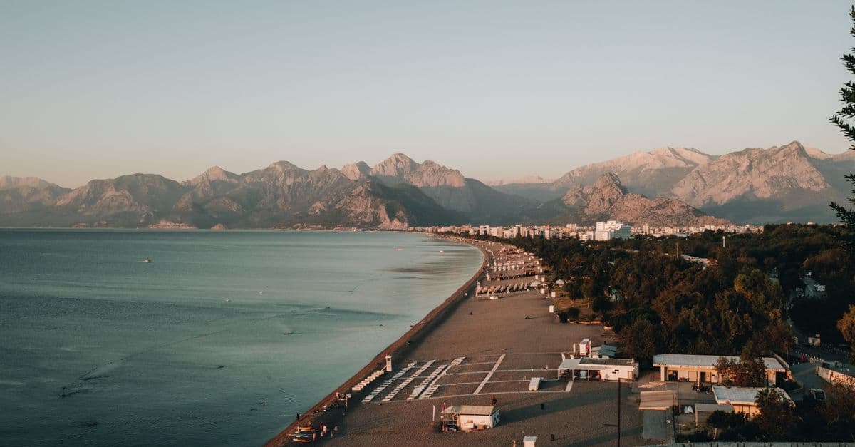 Den långa stranden i Antalya i gryningsljus, med staden och höga berg i bakgrunden.