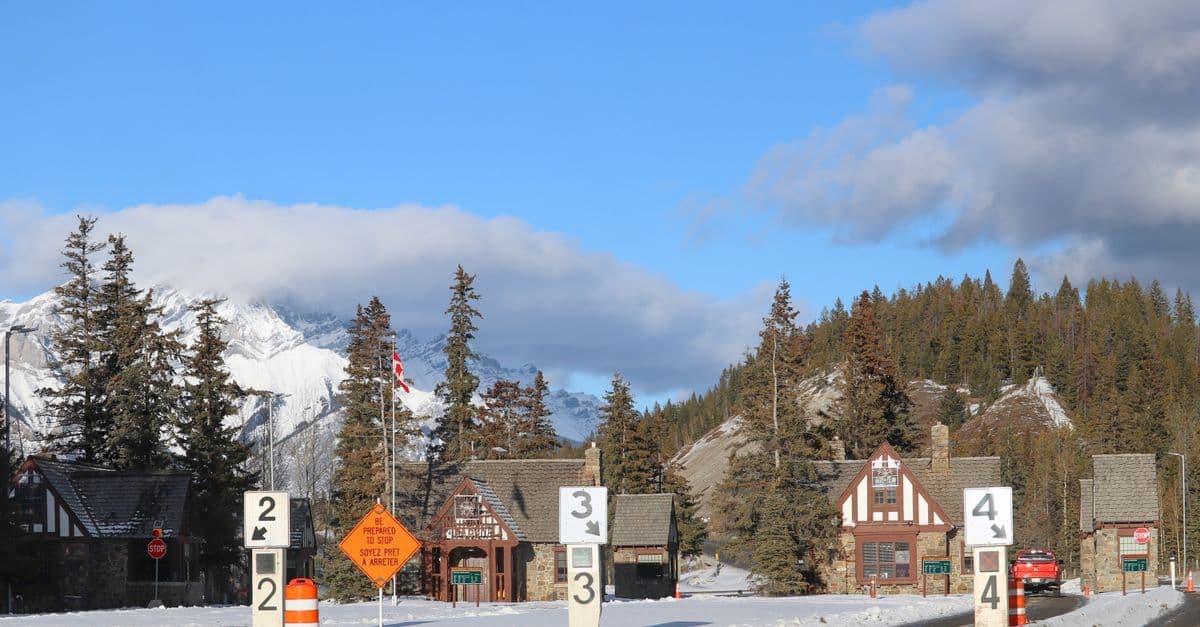 Roadside signs mark lanes 2, 3, and 4 in a mountain village beneath snowy peaks and pine-covered slopes.