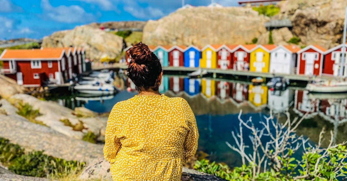 Kvinna i gul blus sitter vid vattnet i Smögen med färgglada båtskjul – skatt och pension är avgörande vid utlandsarbete