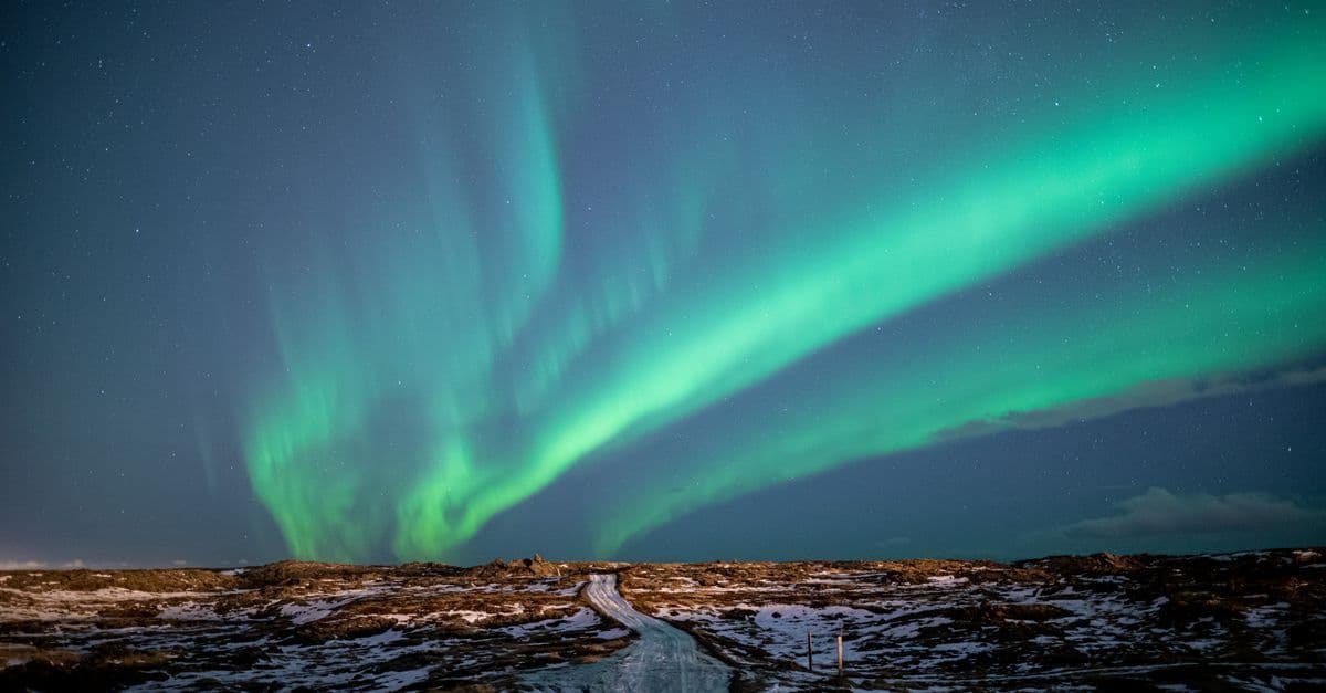 Green northern lights sweep across the night sky above a snowy Icelandic landscape.