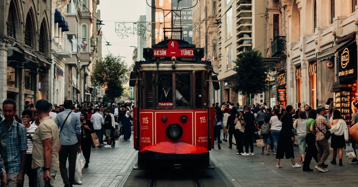 Un tram rosso attraversa una via affollata di Istanbul, tra negozi e palazzi.