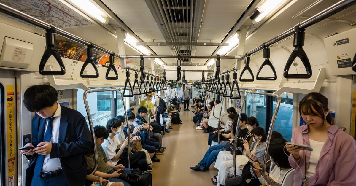 vsモバイルのeSIMに対応したスマートフォンを手に、日本の満員電車に乗る乗客たちの日常風景