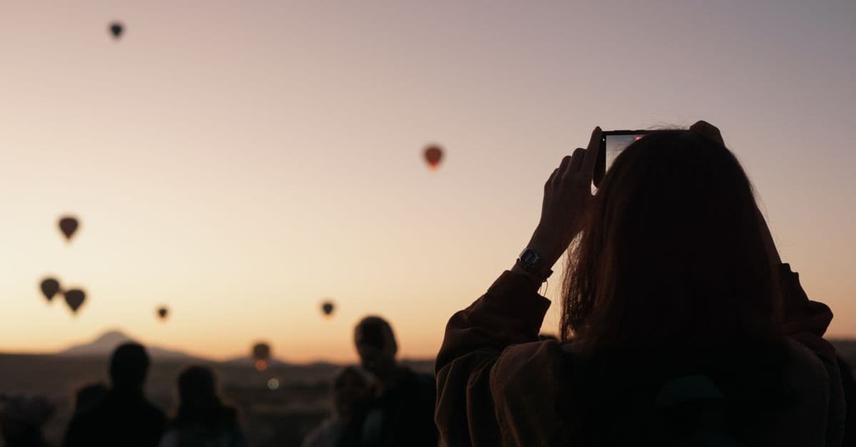Eine Frau fotografiert in Kappadokien bei Sonnenaufgang Heißluftballons mit dem Handy.