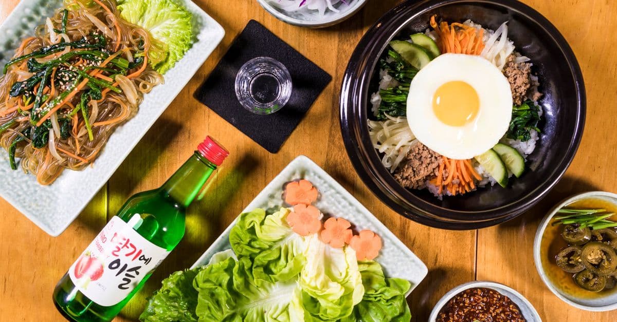 Mâm cơm đồ ăn Hàn Quốc truyền thống với bibimbap, japchae và soju trên bàn gỗ