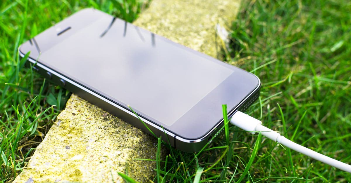 Smartphone with charging cable resting on grass outdoors, exploring connectivity alternatives to roaming charges