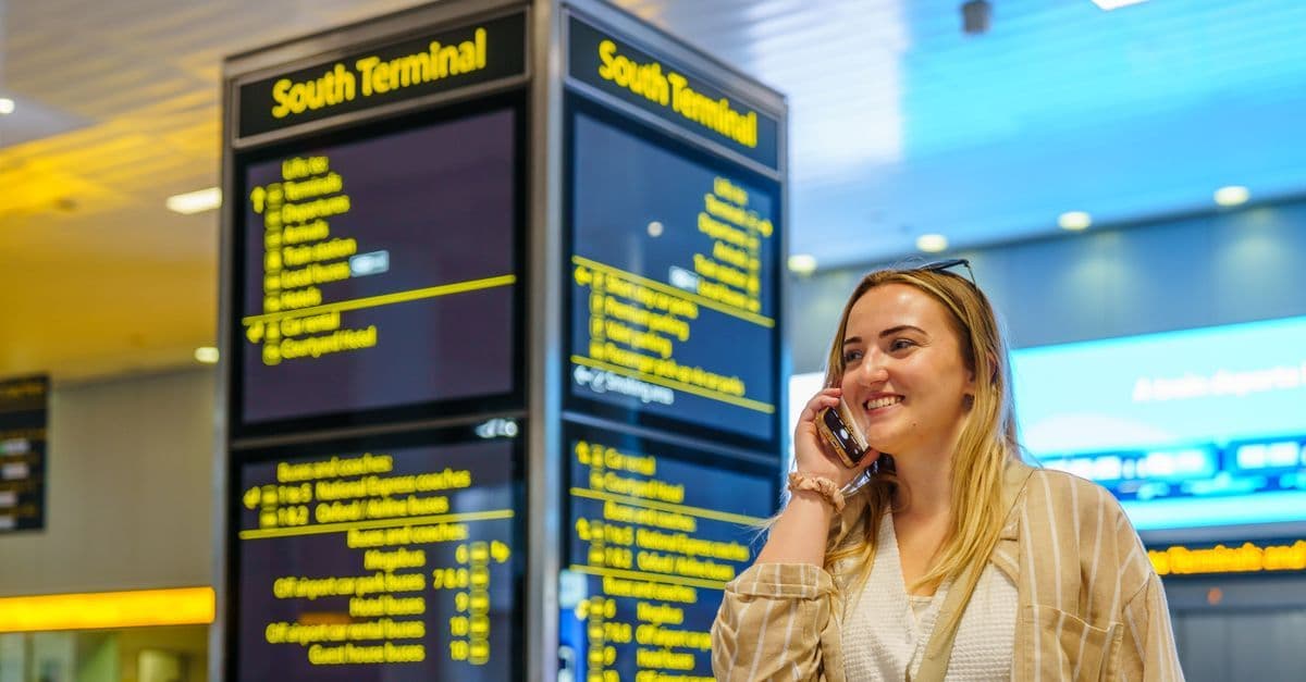 Người phụ nữ vui vẻ dùng eSIM du lịch nước ngoài tại sân bay Gatwick