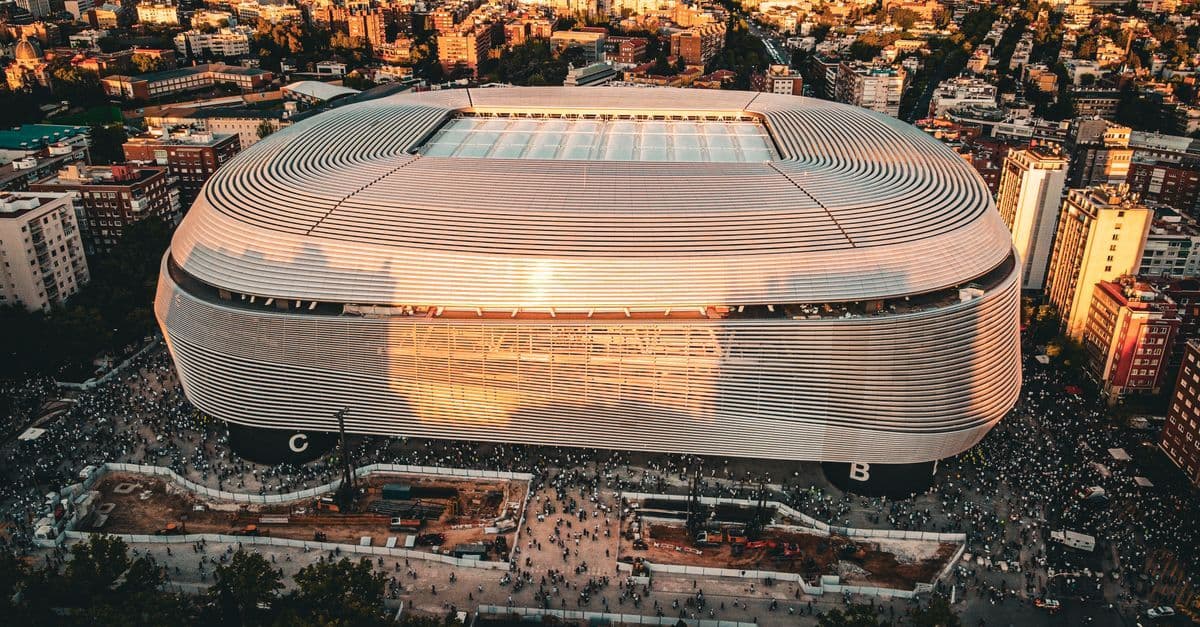 Vista aérea do Estádio Santiago Bernabéu ao pôr do sol, capturando o calor seco do verão em Madrid.