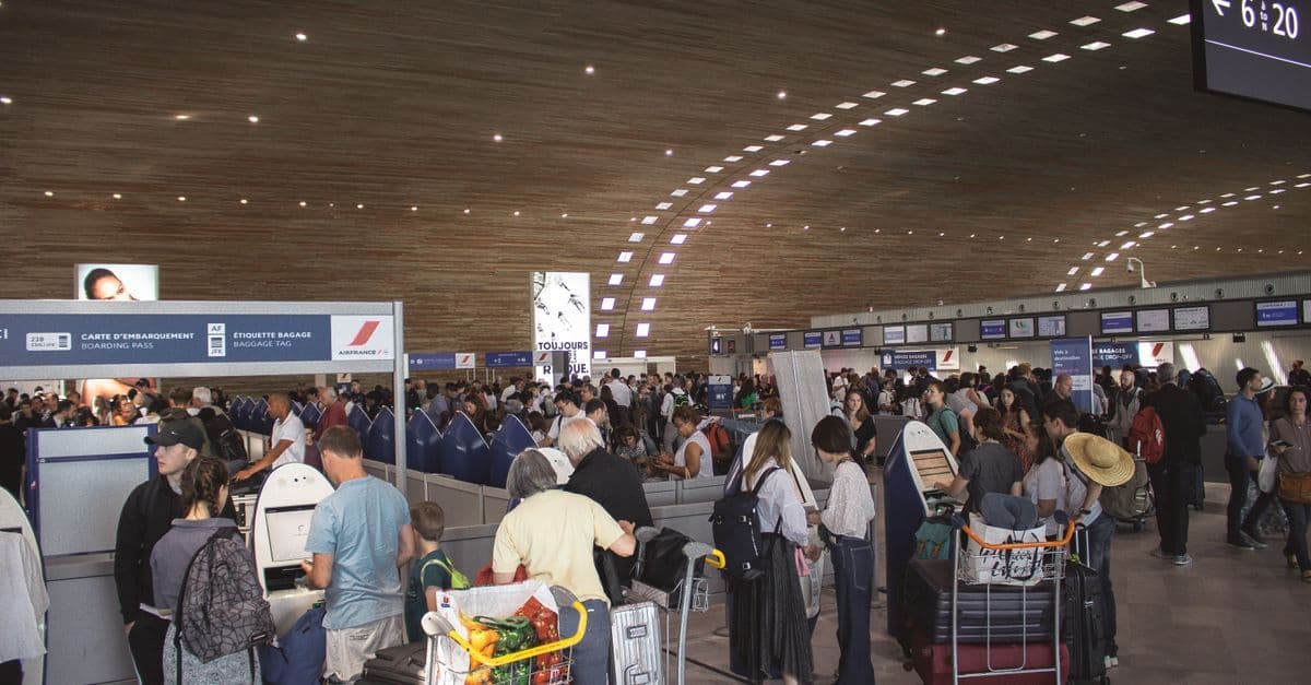 Travelers queue with luggage carts at a busy airport immigration hall.