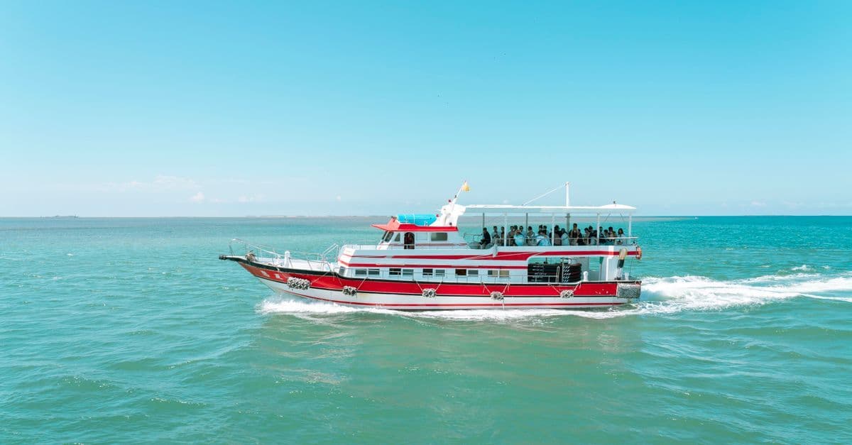 A red-and-white passenger boat cruises across turquoise water beneath a clear blue sky.