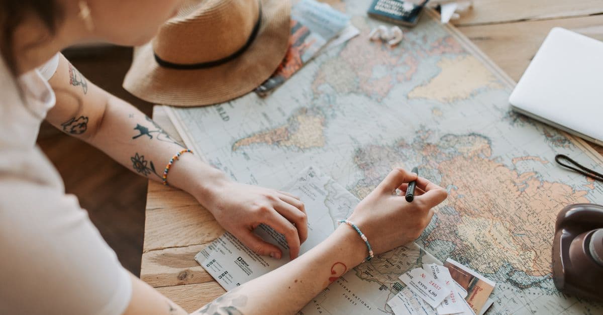 Người lập flight itinerary với bản đồ, hộ chiếu và đồ dùng du lịch trên bàn gỗ.