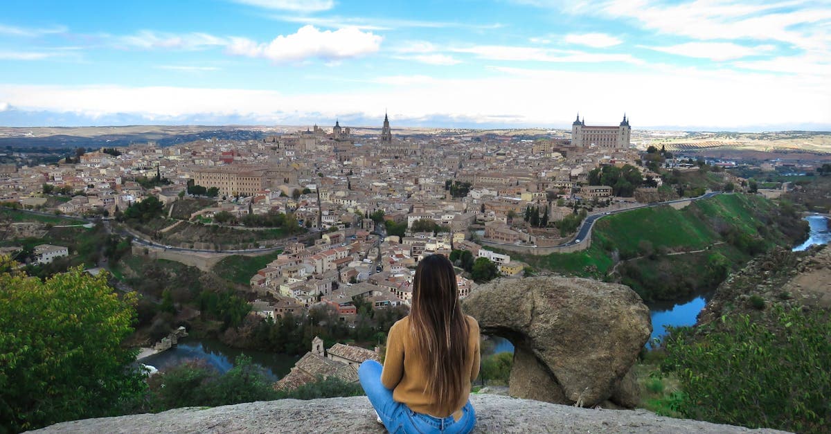 Viajera contemplando el paisaje histórico de Toledo desde un mirador bajo un cielo azul intenso.
