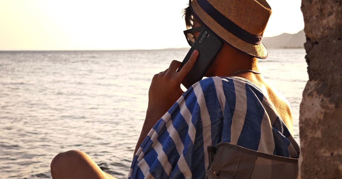 Ein Mann telefoniert im gestreiften Hemd am Meer und genießt die Abendsonne.